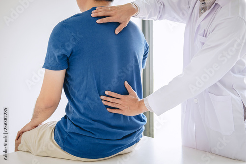 Doctor physiotherapist treating lower back pain patient after while giving exercising treatment on stretching in the clinic, Rehabilitation physiotherapy concept