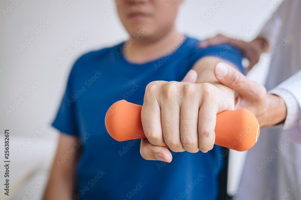 Doctor physiotherapist assisting a male patient while giving exercising treatment on stretching his arm with dumbbell in the clinic, Rehabilitation physiotherapy concept
