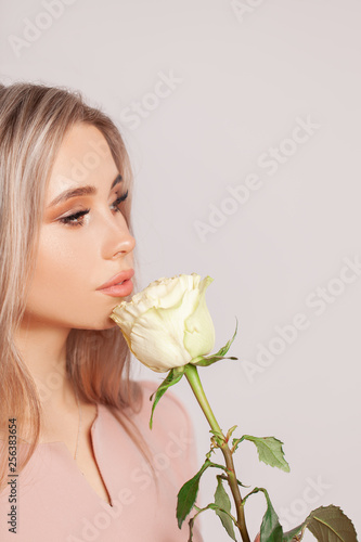 Young woman in pretty pink dress holding rose flower in studio