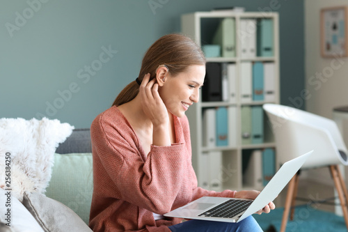 Young woman with hearing aid using laptop at home