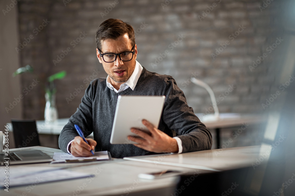 Businessman using touchpad and taking notes on the paper. Businessman using touchpad and taking notes on the paper.