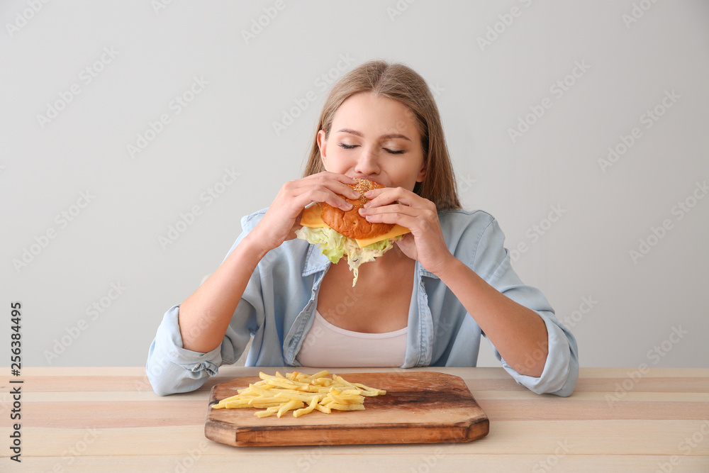 Young woman eating tasty burger with french fries at table Young woman eating tasty burger with french fries at table