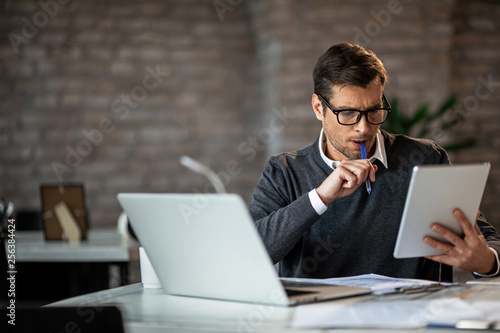 Mid adult businessman using digital tablet while working at his desk in the office.