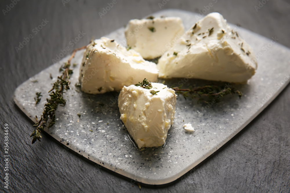 Board with tasty feta cheese and thyme on dark table