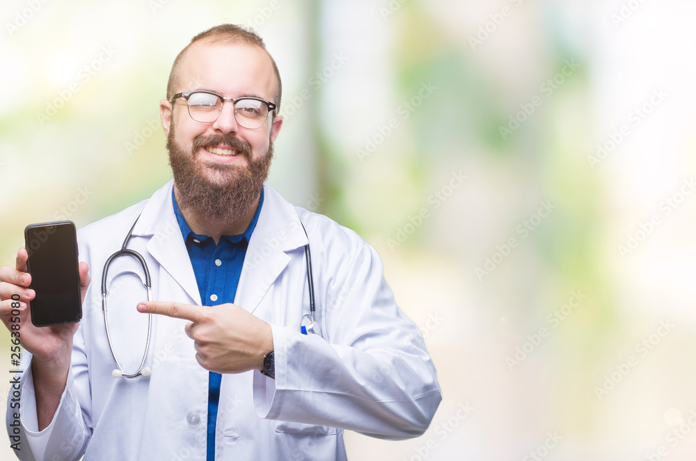 Young doctor man showing smartphone screen over isolated background very happy pointing with hand and finger Young doctor man showing smartphone screen over isolated background very happy pointing with hand and finger