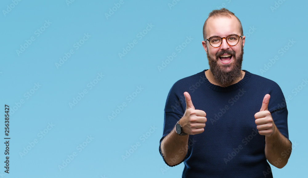 Young caucasian hipster man wearing sunglasses over isolated background approving doing positive gesture with hand, thumbs up smiling and happy for success. Looking at the camera, winner gesture. Young caucasian hipster man wearing sunglasses over isolated background approving doing positive gesture with hand, thumbs up smiling and happy for success. Looking at the camera, winner gesture.