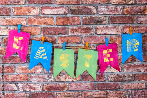 Colorfull handmade flags with letters , inscription Easter , against a red brick wall