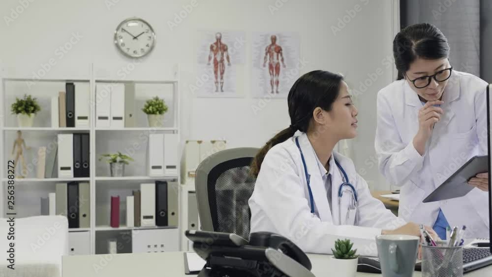 slow motion of positive young female intern asking advice from asian woman doctor at clinic reception. two healthcare staff discuss with coworker for opinion while examine x-ray of patient on tablet slow motion of positive young female intern asking advice from asian woman doctor at clinic reception. two healthcare staff discuss with coworker for opinion while examine x-ray of patient on tablet