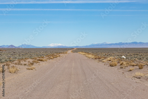A long dusty road in the Nevada desert  with a snowcapped mountain in the distance