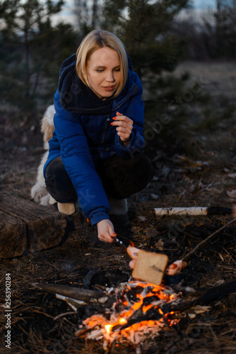 A woman is cooking sausage on a fire in nature. Camping, picnic concept.