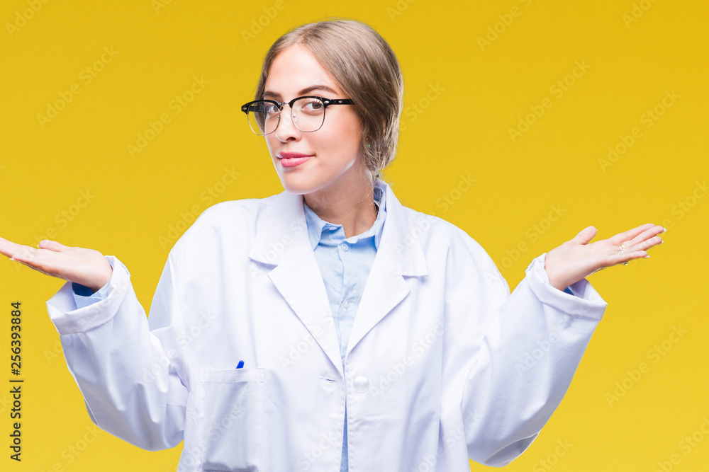 Beautiful young blonde doctor woman wearing white coat over isolated background clueless and confused expression with arms and hands raised. Doubt concept. Beautiful young blonde doctor woman wearing white coat over isolated background clueless and confused expression with arms and hands raised. Doubt concept.