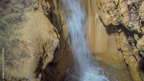 A waterfall is falling down in a cave Pekel in Slovenia. There is a small lake on the ground. photo