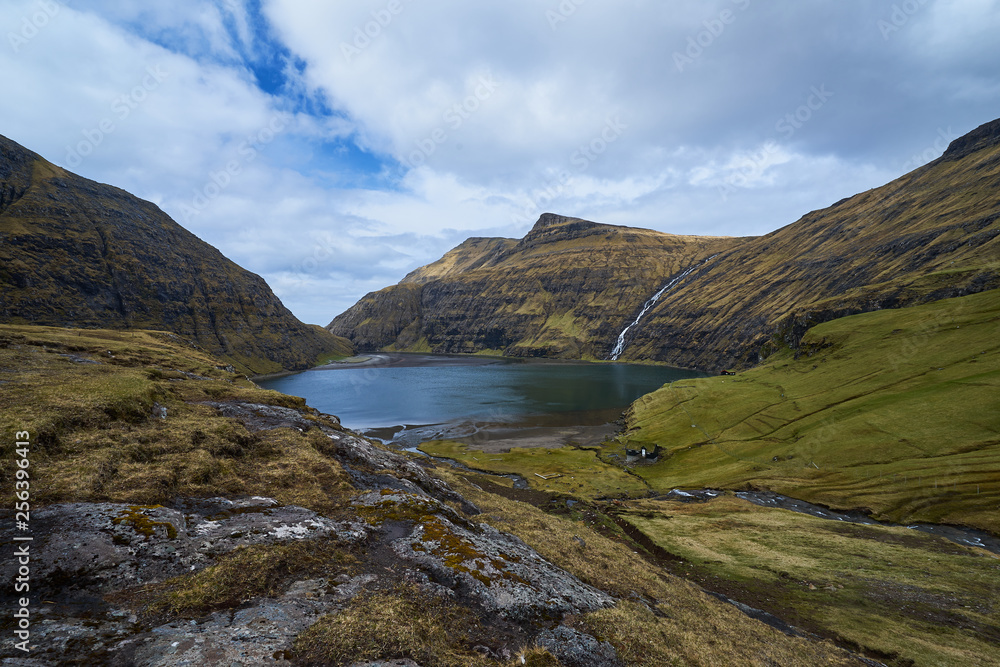 Scenic landscape picture on sea water lagoon or lake between mountains without trees in willage Saksun or danish Saksen in faroese island Streymoy in north atlantic in spring sunny, cloudy morning. 