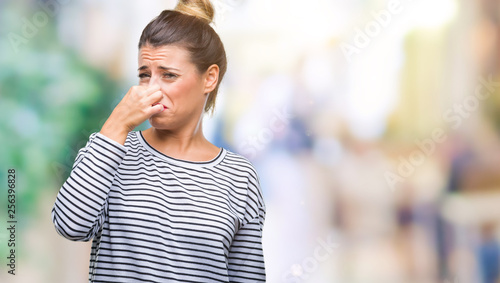 Young beautiful woman casual stripes sweater over isolated background smelling something stinky and disgusting, intolerable smell, holding breath with fingers on nose. Bad smells concept.