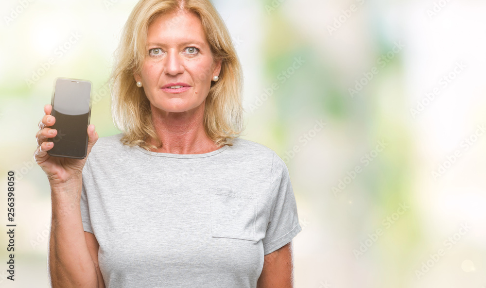 Middle age blonde woman showing blank screen of smartphone over isolated background with a confident expression on smart face thinking serious Middle age blonde woman showing blank screen of smartphone over isolated background with a confident expression on smart face thinking serious