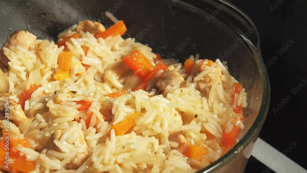 Glass pan with steaming pilaf close-up. Boiled rice with carrots and meat steaks standing on the stove Glass pan with steaming pilaf close-up. Boiled rice with carrots and meat steaks standing on the stove