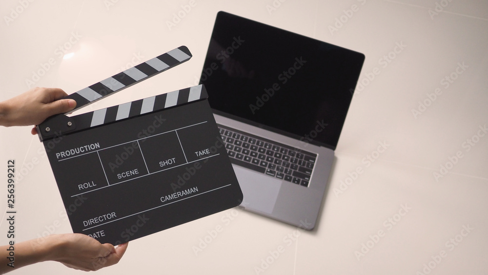 Hand is holding Black Movie slate or clapperboard and laptop use in video production ,film, cinema industry on white background.