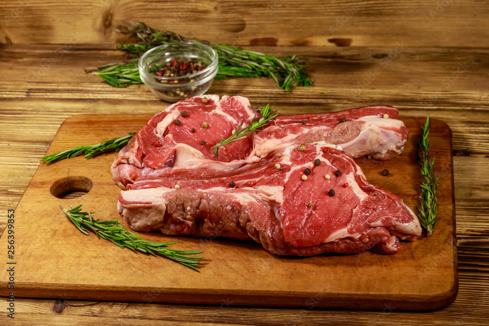 Raw fresh beef rib eye steaks on bone with spices and rosemary on wooden table