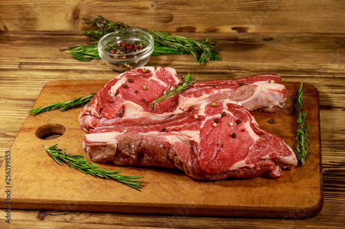 Raw fresh beef rib eye steaks on bone with spices and rosemary on wooden table