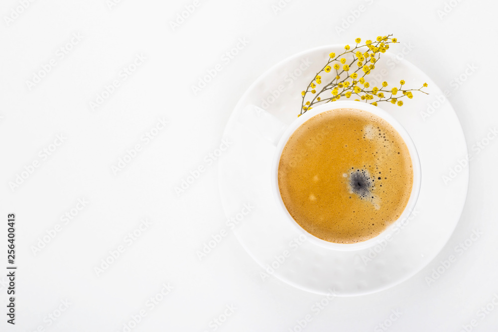 White cup of coffee on a white table with yellow mimosa flowers. Minimalism. Top view, flat lay White cup of coffee on a white table with yellow mimosa flowers. Minimalism. Top view, flat lay