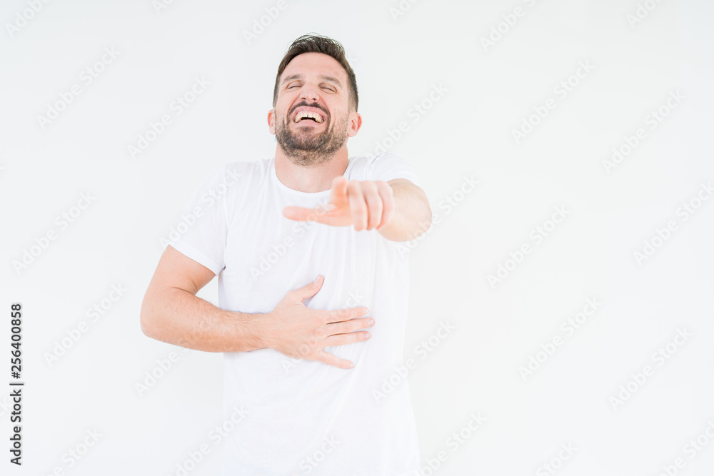 Young handsome man wearing casual white t-shirt over isolated background Laughing of you, pointing to the camera with finger hand over chest, shame expression Young handsome man wearing casual white t-shirt over isolated background Laughing of you, pointing to the camera with finger hand over chest, shame expression