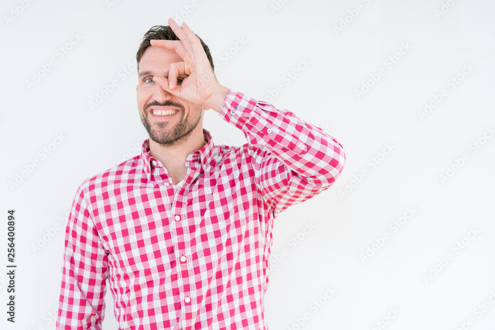 Fototapeta premium Young handsome man wearing shirt over isolated background doing ok gesture with hand smiling, eye looking through fingers with happy face.