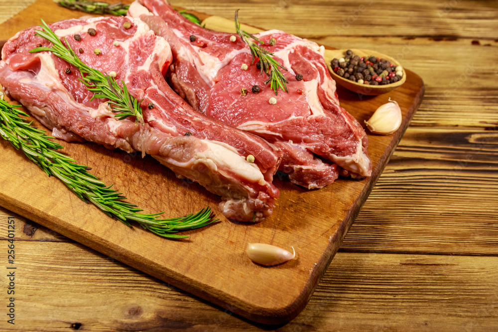 Raw fresh beef rib eye steak on bone with spices, garlic and rosemary on wooden table