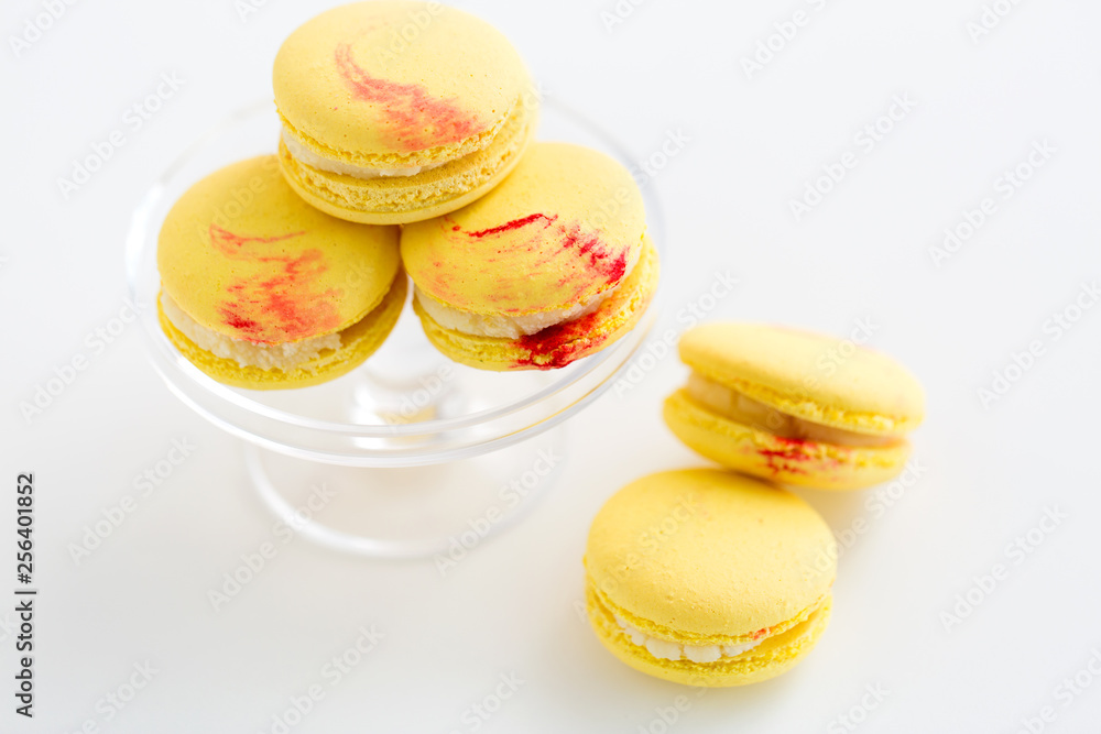 sweets, pastry and food concept - close up of lemon yellow macarons on glass confectionery stand over white background sweets, pastry and food concept - close up of lemon yellow macarons on glass confectionery stand over white background