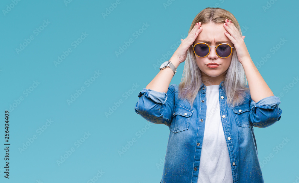 Young blonde woman wearing sunglasses over isolated background suffering from headache desperate and stressed because pain and migraine. Hands on head. Young blonde woman wearing sunglasses over isolated background suffering from headache desperate and stressed because pain and migraine. Hands on head.