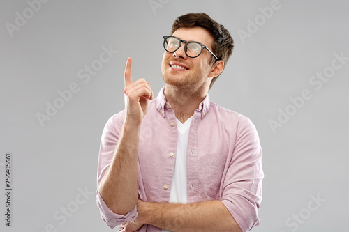 education, idea and people concept - smiling young man in glasses pointing finger up over grey background