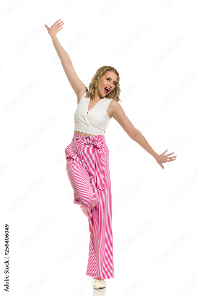 Carefree Woman In Striped Wide Legs Trousers Is Standing On One Leg With Arms Outstretched Carefree Woman In Striped Wide Legs Trousers Is Standing On One Leg With Arms Outstretched