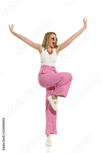 Happy Woman In Striped Wide Legs Trousers Is Standing On One Leg With Arms Outstretched And Shouting