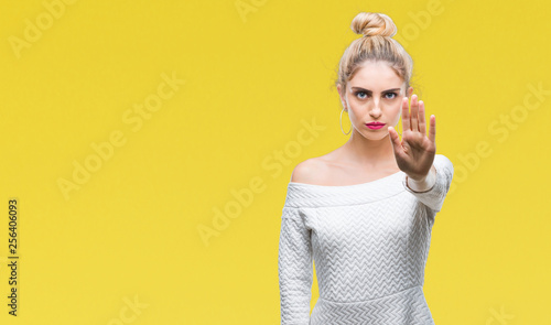 Young beautiful blonde and blue eyes woman over isolated background doing stop sing with palm of the hand. Warning expression with negative and serious gesture on the face.