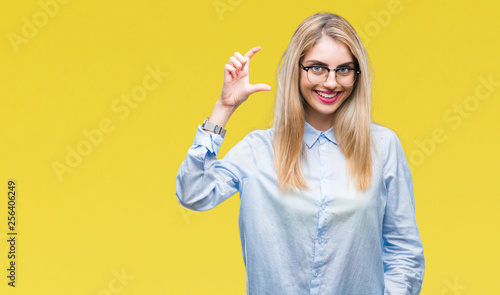Young beautiful blonde business woman wearing glasses over isolated background smiling and confident gesturing with hand doing size sign with fingers while looking and the camera. Measure concept.