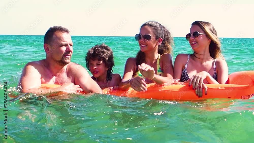 Happy family of four in vacation at sea shore. Happy family with yellow mattress bathes in sea. happy mum daddy and two children play in water. Slow Motion Happy family of four in vacation at sea shore. Happy family with yellow mattress bathes in sea. happy mum daddy and two children play in water. Slow Motion