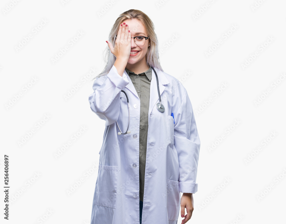Young blonde doctor woman over isolated background covering one eye with hand with confident smile on face and surprise emotion. Young blonde doctor woman over isolated background covering one eye with hand with confident smile on face and surprise emotion.