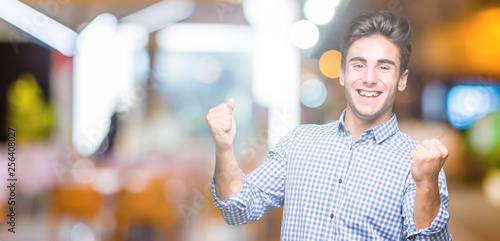Young handsome business man over isolated background very happy and excited doing winner gesture with arms raised, smiling and screaming for success. Celebration concept.