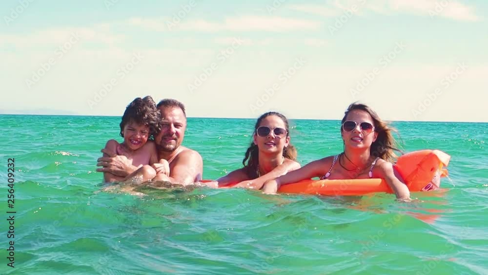 Happy family of four in vacation at sea shore. Happy family with yellow mattress bathes in sea. happy mum daddy and two children play in water. Slow Motion Happy family of four in vacation at sea shore. Happy family with yellow mattress bathes in sea. happy mum daddy and two children play in water. Slow Motion