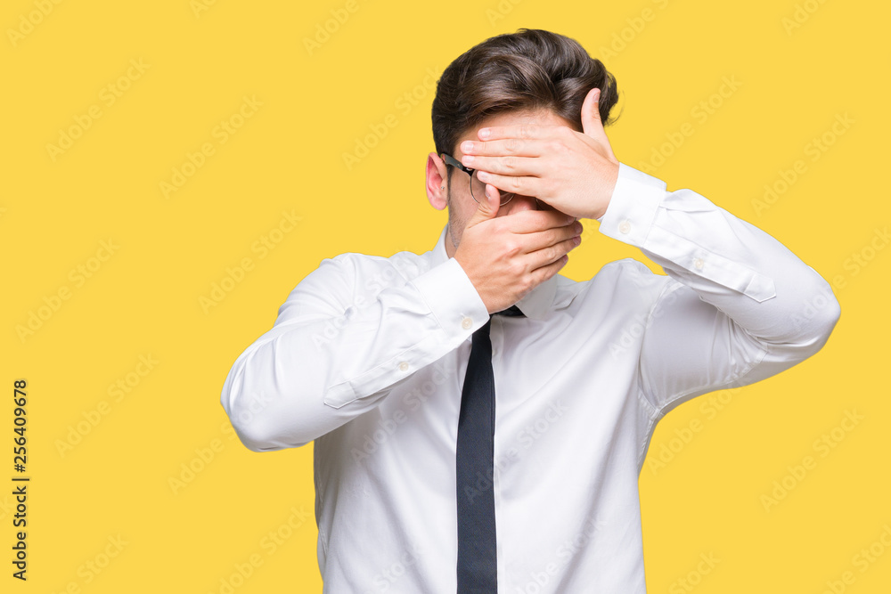 Young business man wearing glasses over isolated background Covering eyes and mouth with hands, surprised and shocked. Hiding emotion