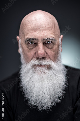 studio portrait of a bald man with tattooed arms and white beard