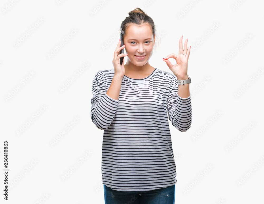 Young beautiful caucasian woman talking on smartphone over isolated background doing ok sign with fingers, excellent symbol Young beautiful caucasian woman talking on smartphone over isolated background doing ok sign with fingers, excellent symbol