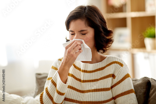 healthcare, cold, allergy and people concept - sick woman blowing her runny nose in paper tissue at home photo