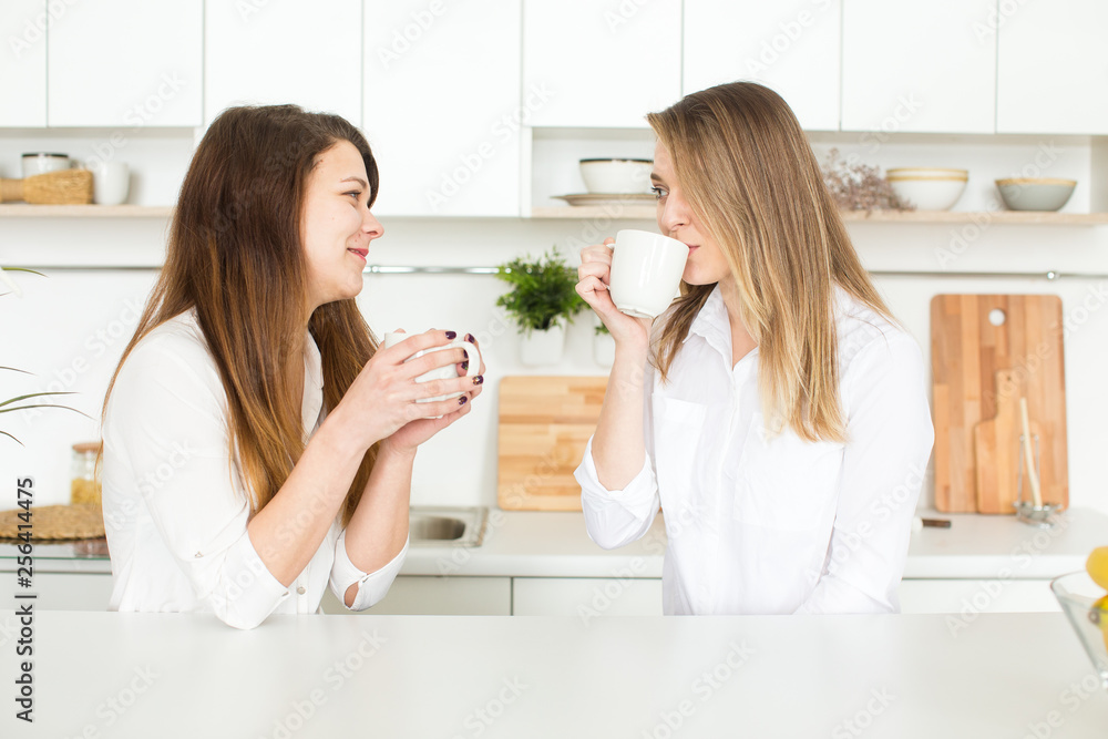 Two best friends girls having fun drink coffee, smiling and gossip, joyful sisters celebrating birthday party, elegant stylish clothes Two best friends girls having fun drink coffee, smiling and gossip, joyful sisters celebrating birthday party, elegant stylish clothes