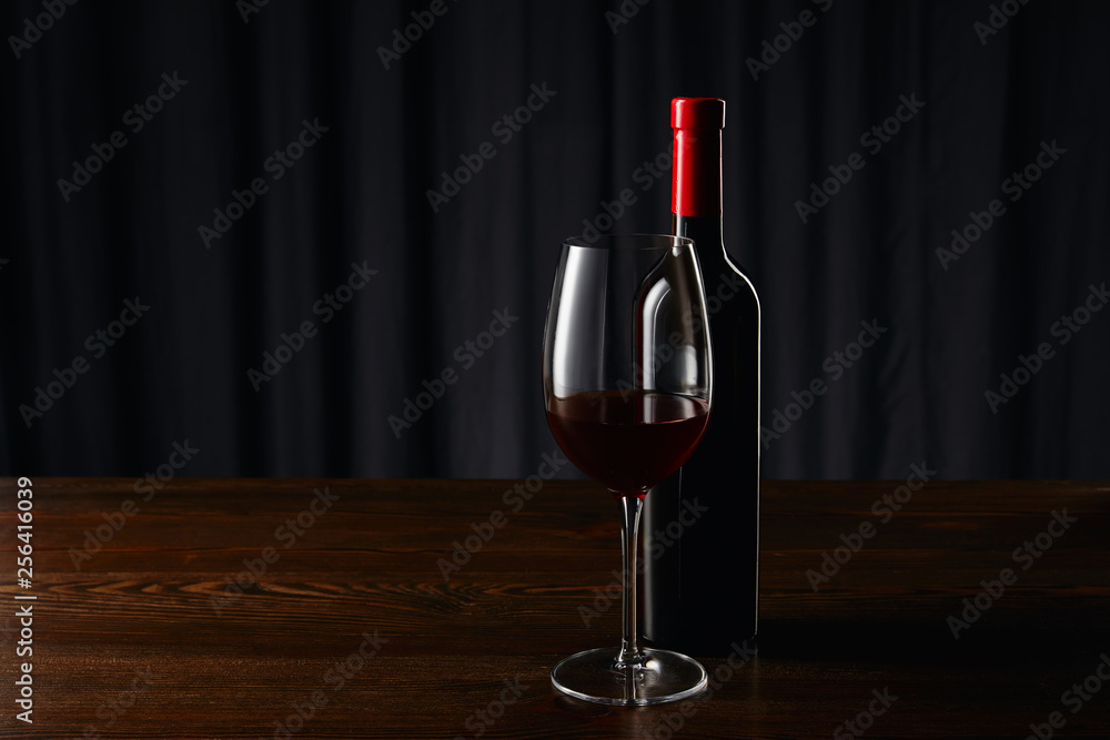 Wine bottle and glass with red wine on wooden surface