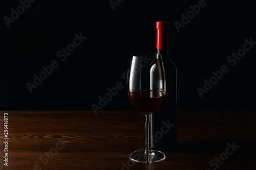 Bottle and glass of red wine on wooden surface isolated on black