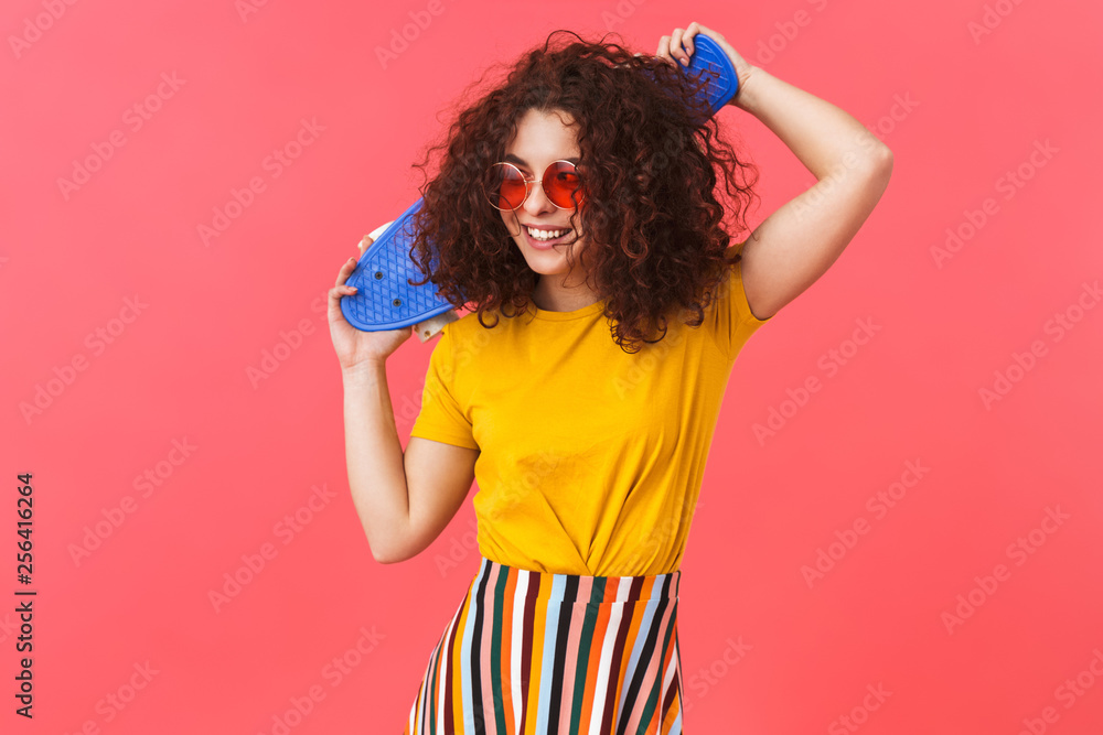 Beautiful young curly girl posing isolated over red wall background with skateboard. Beautiful young curly girl posing isolated over red wall background with skateboard.