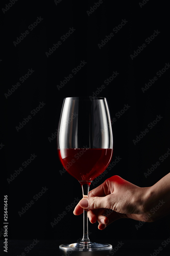 Partial view of woman holding wine glass with red wine isolated on black Partial view of woman holding wine glass with red wine isolated on black