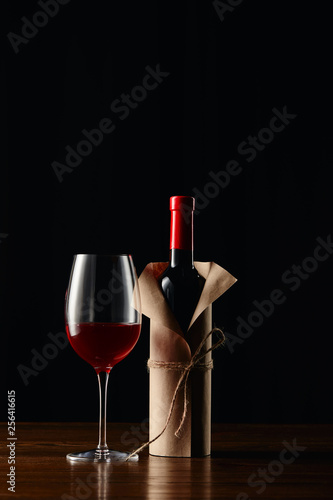 Wine glass and bottle in paper wrapper on wooden surface isolated on black