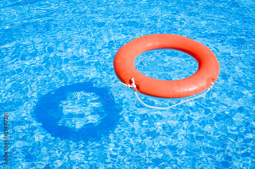 Closeup view of a red ring life buoy and its shadow floating on the blue water of the swimming pool during a sunny summer day