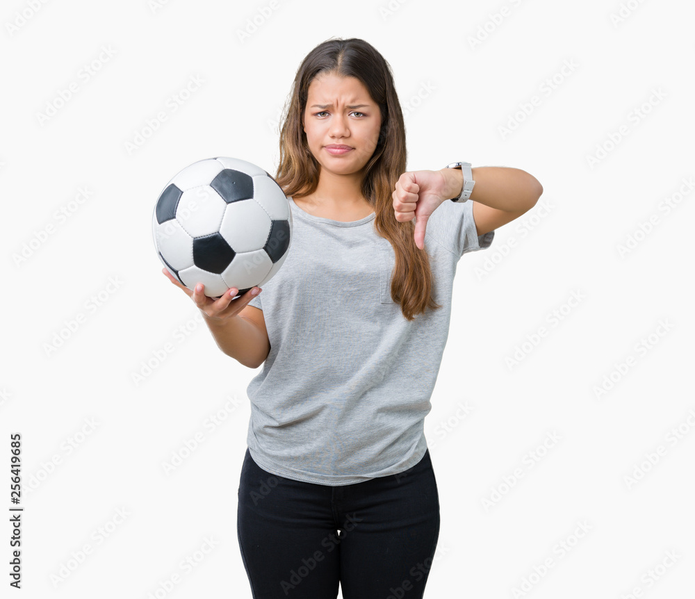 Young beautiful brunette woman holding soccer football ball over isolated background with angry face, negative sign showing dislike with thumbs down, rejection concept Young beautiful brunette woman holding soccer football ball over isolated background with angry face, negative sign showing dislike with thumbs down, rejection concept
